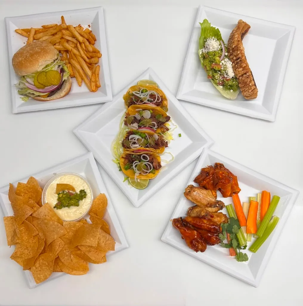 A spread of plates from the kitchen: burger and fries, tacos, wings, chips and queso