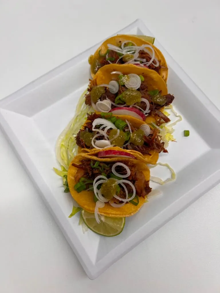 Tacos on a white plate with onion, radish and lime